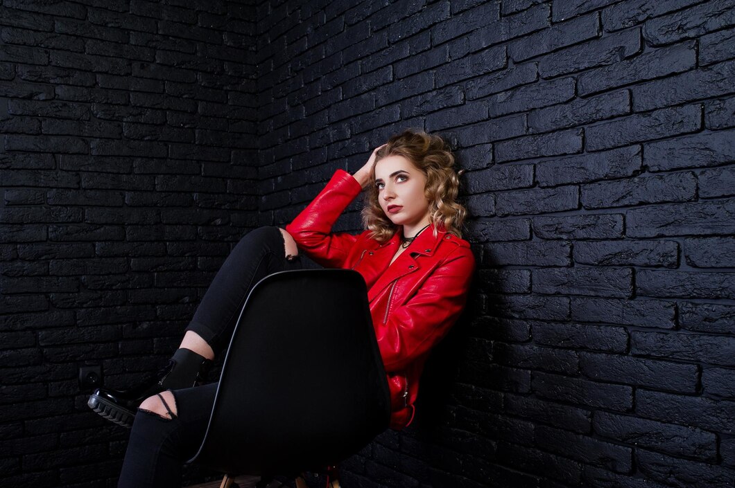 studio-portrait-blonde-girl-red-leather-jacket-posed-chair-against-brick-wall